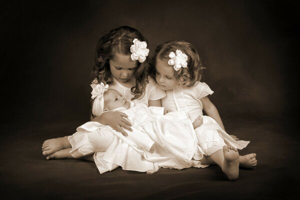 Two girls in white are holding a baby in their arms