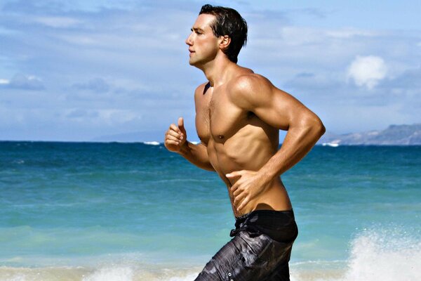 Спортивный мужчина бежит по пляжу