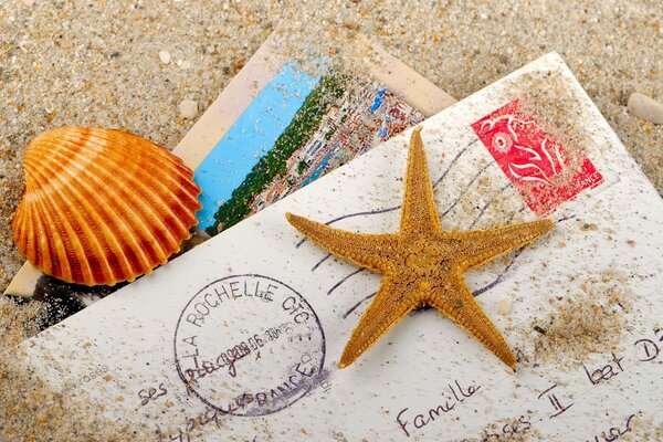 Brief mit Postkarte im Sand mit Muscheln