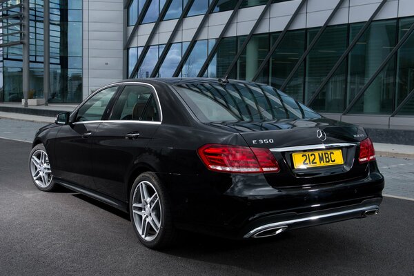Mercedes-Benzes e 350 черный припаркован дороге рядом с офисным зданием