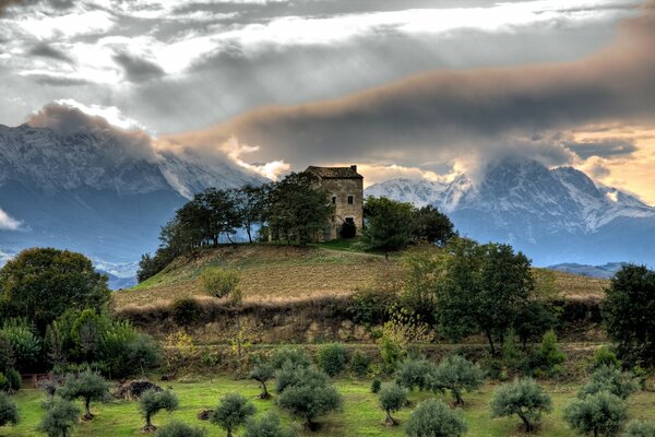 Gewitterwolken , Bäume und ein Haus auf einem Hügel