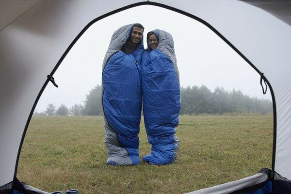 A couple in love in sleeping bags is standing in front of the tent
