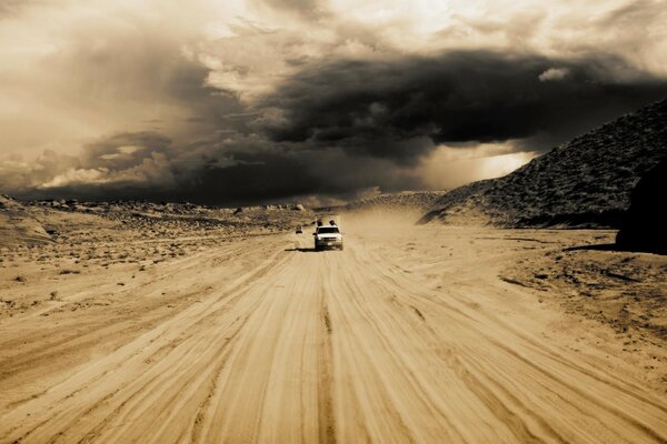 Carro se move no deserto na areia contra o pôr do sol