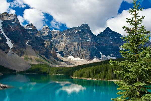 Clouds caught on mountain peaks. Clean lake at the foot of the mountains. Green spruce. Protected area