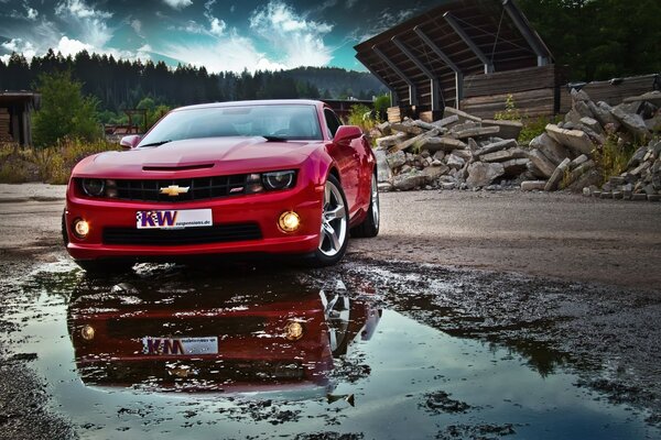 Red Chevrolet and its reflection in a puddle on the background of mountains