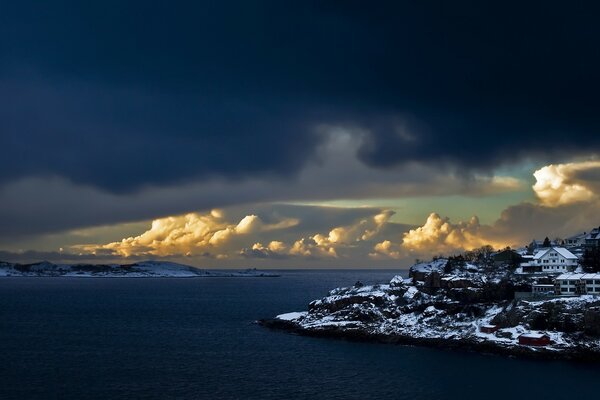 Houses on the snowy shore against the background of huge clouds