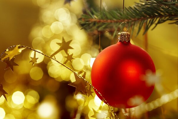 Foto borrosa bola roja de Navidad de juguete en el fondo de oro