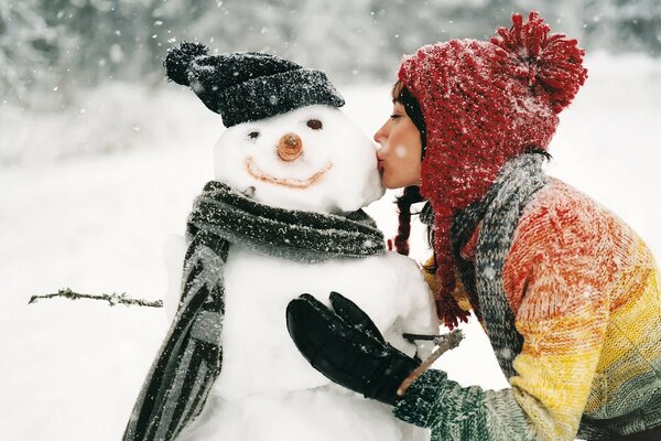 Mädchen küsst einen Schneemann in einer Mütze