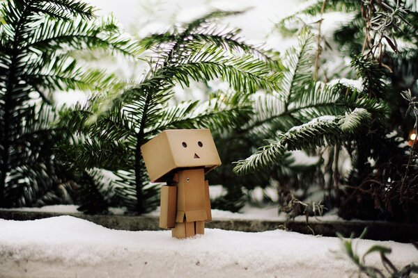 A robot made of cardboard boxes stands in the snow among the fir branches