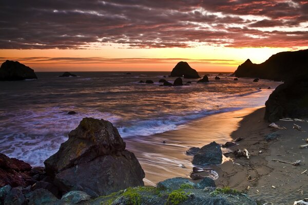 Tramonto vicino all oceano. Spiaggia serale con rocce e onde