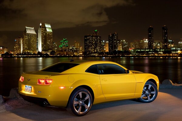 Chevrolet amarelo com faróis ligados no fundo da cidade noturna