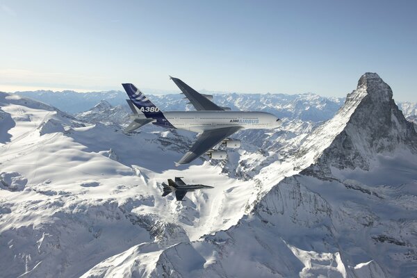 An airliner and a fighter jet flying over snowy mountains