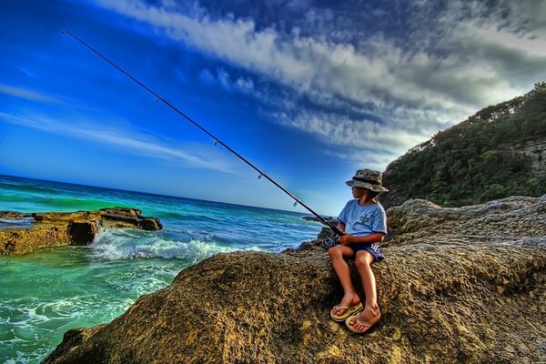 A boy is fishing on the shore of a rocky coast