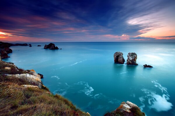 Vista della superficie del mare che scorre oltre il bordo dell orizzonte serale, due rocce solitarie che si affacciano l una sull altra