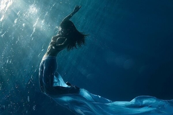 A girl in a transparent robe under water in a set of sunny rays