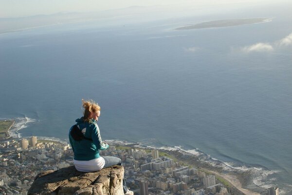 A girl is sitting on a rock above the sea