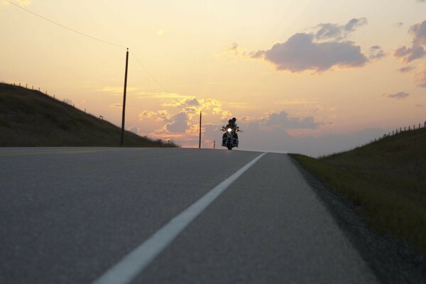 A couple of people on a motorcycle ride along the road going into the sunset