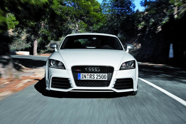 A white Audi is driving on the road