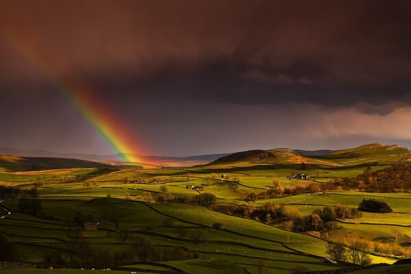 Regenbogen bei Sonnenuntergang in einem hügeligen Feld