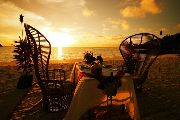 Dîner pour deux sur la plage sous le coucher de soleil au bord de la mer