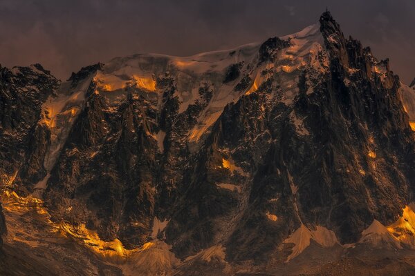 The snow-capped top of the mountain in the rays of the setting sun