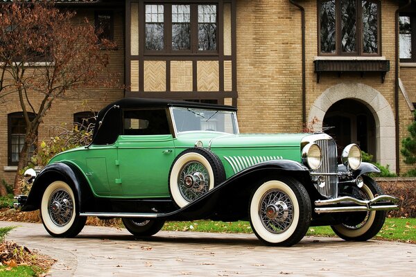 Une voiture de Tourisme du début du 20ème siècle de couleur verte avec un cabriolet et deux passagers