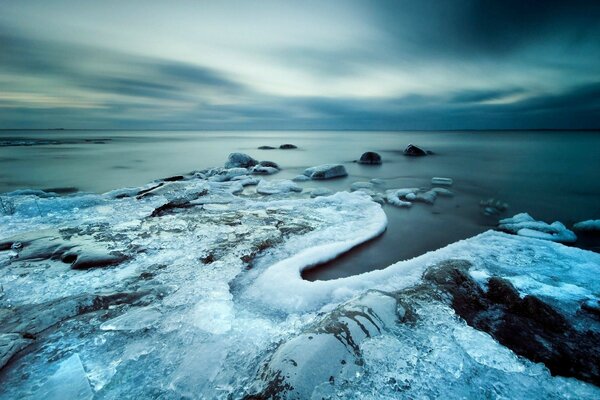 Eine Landschaft von gefrorenen Steinen im Eis. Sonnenuntergang am Wintermeer