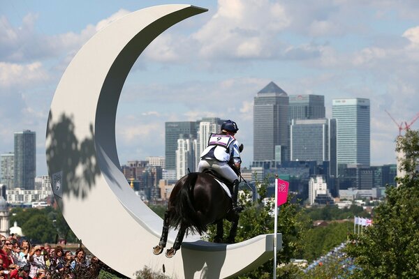 A rider on a black stallion overcomes an obstacle in the form of a young moon