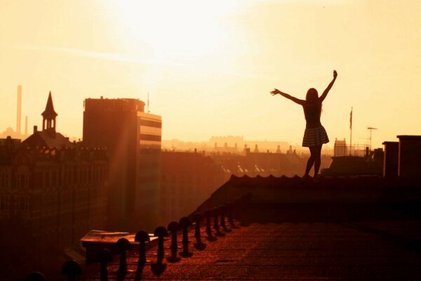 The girl walks along the edge of the roof with her hands raised