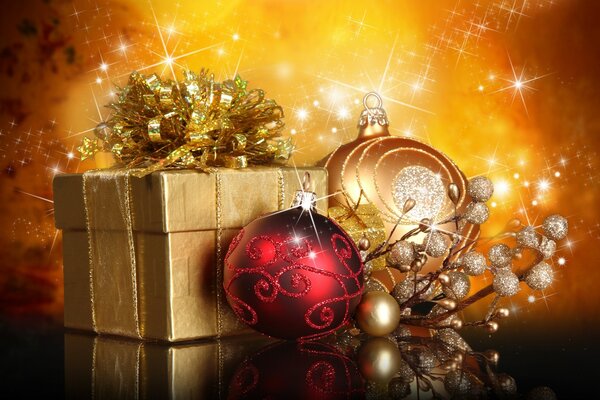 A Christmas gift wrapped in gold paper and a pair of Christmas balls on a background of lights