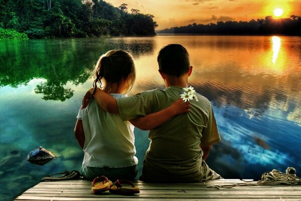 A boy and a girl hugged on the riverbank and look at the sunset