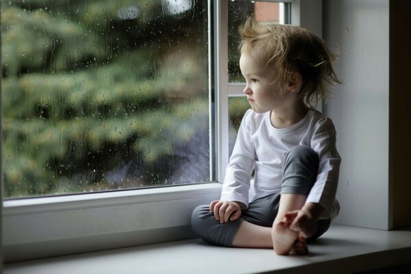 Niña se sienta en el alféizar de la ventana y Mira por la ventana