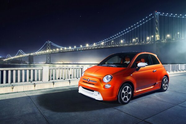 Orange car on the edge of the road on the background of the bridge