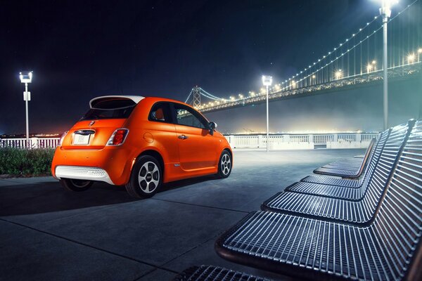 Coche naranja aparcado en el paseo marítimo con vistas al puente