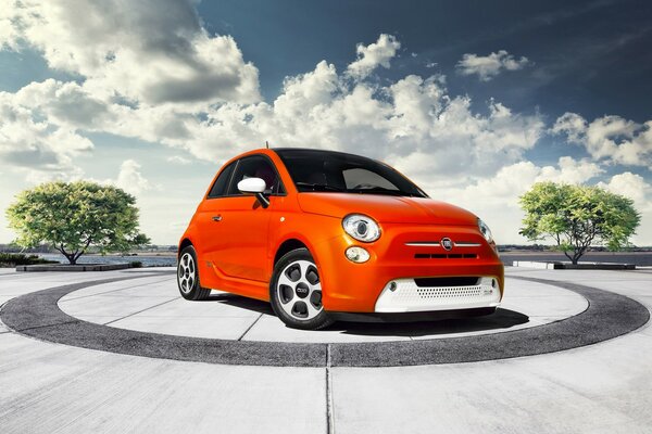 Orange kleiner Fiat in der Mitte eines Kreises auf einem Hintergrund des bewölkten Himmels