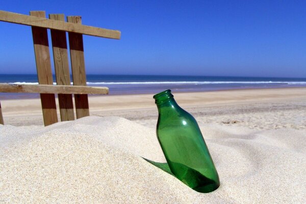 Botella verde sobre fondo de arena blanca