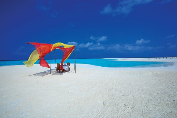 طاولة رومانسية على شاطئ مهجور مع الرمال البيضاء والبحر الأزرق