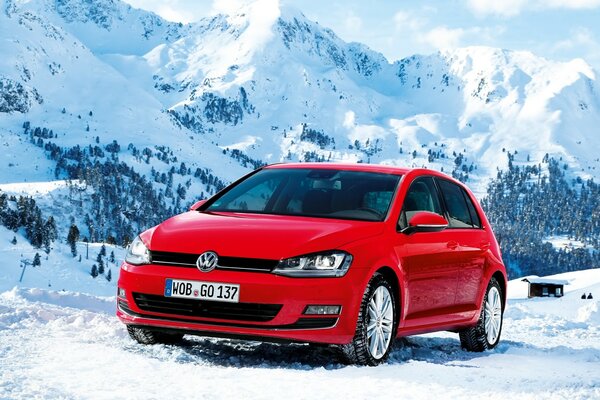 Un auto Volkswagen rossa si trova sulla neve sullo sfondo delle montagne