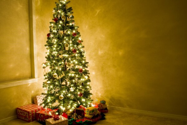 Un albero di Natale alla luce delle luci che tiene sotto di sé scatole con regali