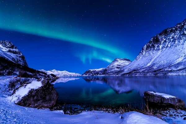 Arctic landscape of a frozen mountain lake in snow-covered shores under the sky with the Northern lights