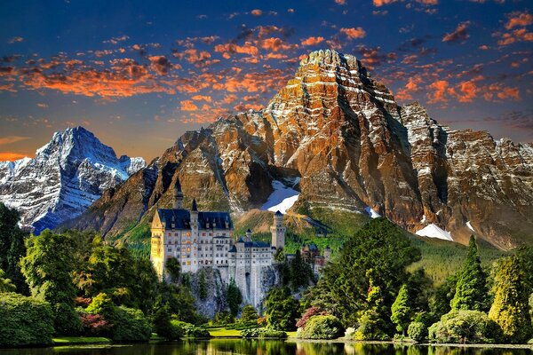 Paesaggio di montagna con il castello e gli alberi con le nuvole rosse nel cielo