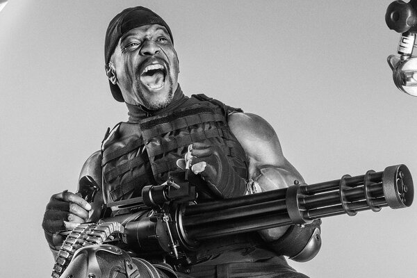 A dark-skinned guy in a cap and a bulletproof vest holds a machine gun