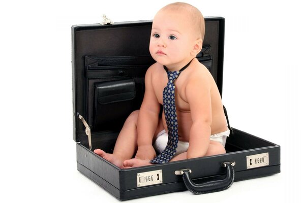 A kid in a tie is sitting in a suitcase