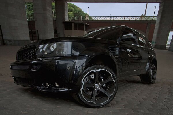 Чёрный автомобиль-внедорожник под мостом с повёрнутыми передними колёсами