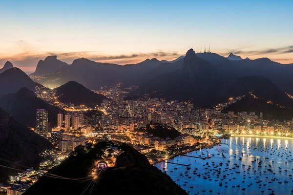 Pôr do sol brilhante sobre as luzes brilhantes da cidade no terreno montanhoso