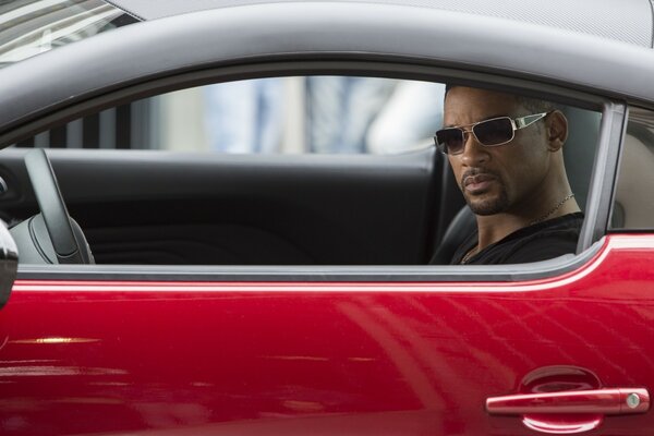 A man in dark glasses, driving a car