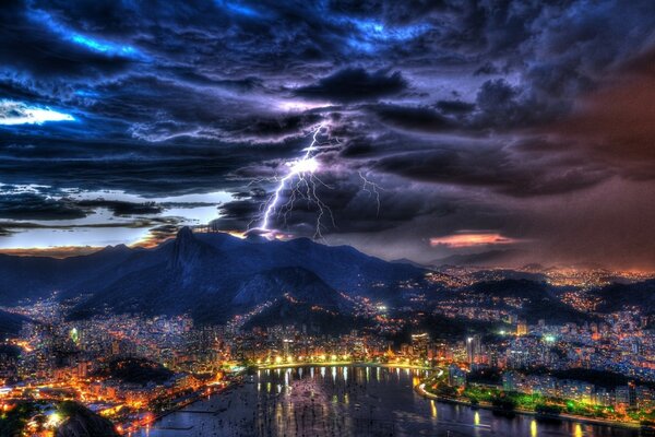 Relámpago brillante en el cielo nocturno sobre la ciudad al pie de la montaña