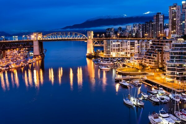 Pont sur la rivière reliant les parties de la ville de nuit dans les lumières sur fond de montagne dans le brouillard blanc