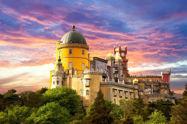 A big beautiful castle on a mountain against a pink-blue sky at sunset