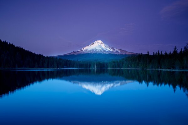 The landscape is a large lake surrounded by a forest and in the distance a high mountain